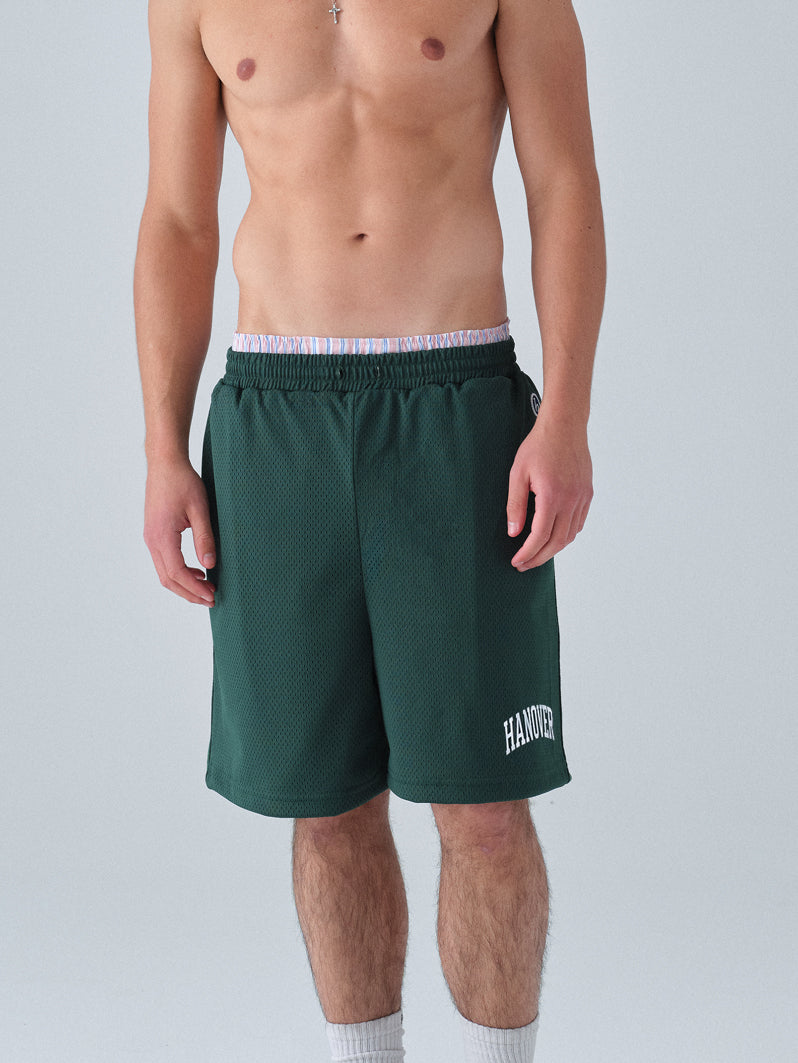 Person wearing green shorts with 'HANOR' branding on a plain background