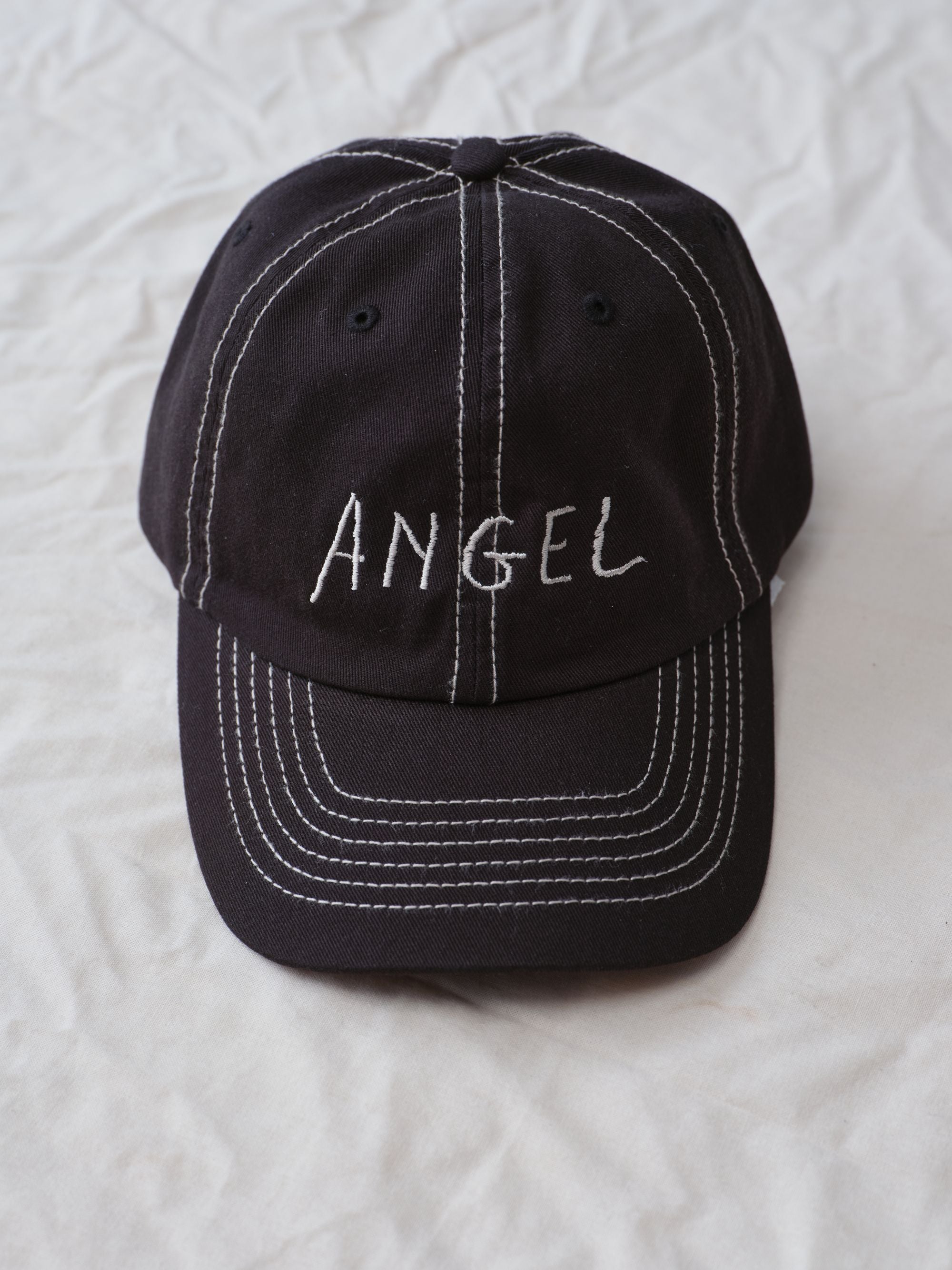 Hanover Angel contrast stitch hat on white textured background flat lay with 'Angel' embroidery 
