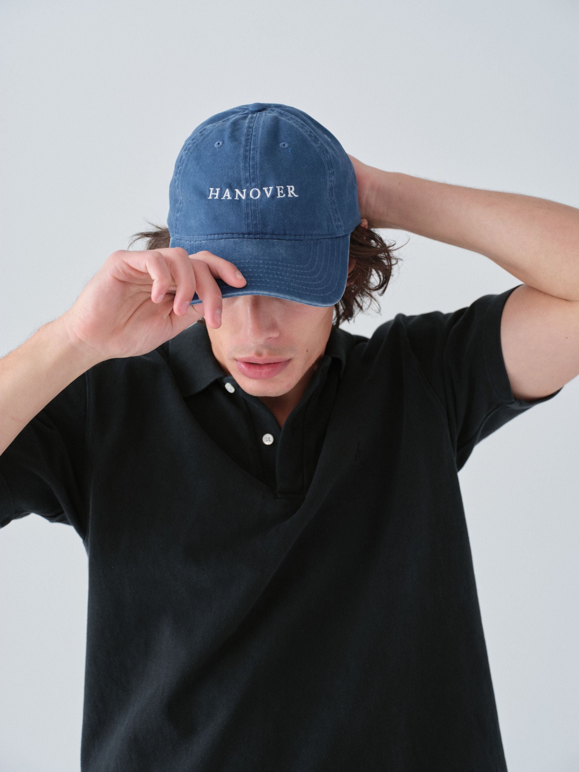 model wearing Sunwashed Staple Polo Shirt in vintage black color and a washed navy Hanover Classic hat