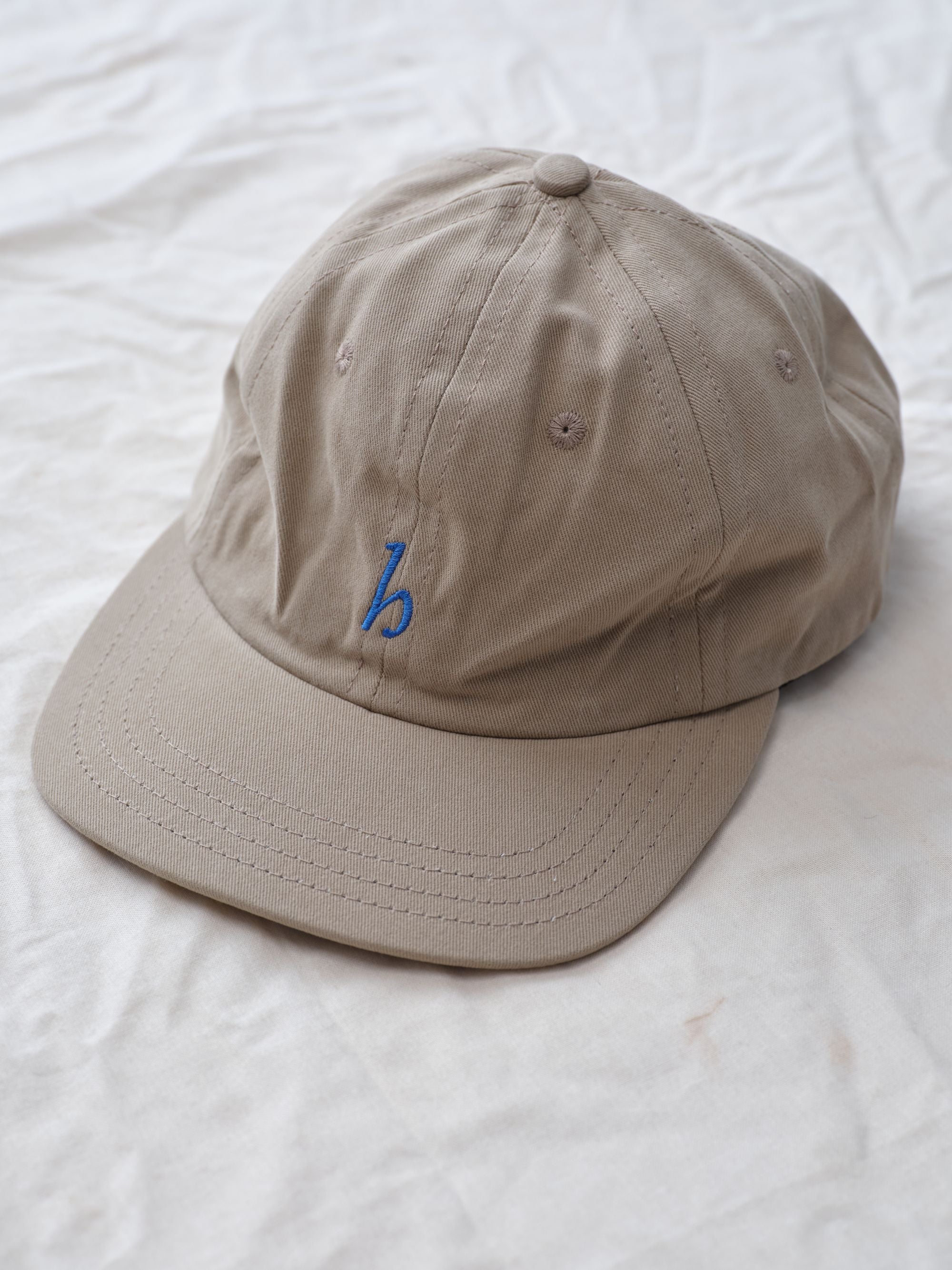 Hanover cap in khaki on textured background alternate view Hanover Cap in cotton twill worn by a young man, showcasing unstructured design and logo embroidery.