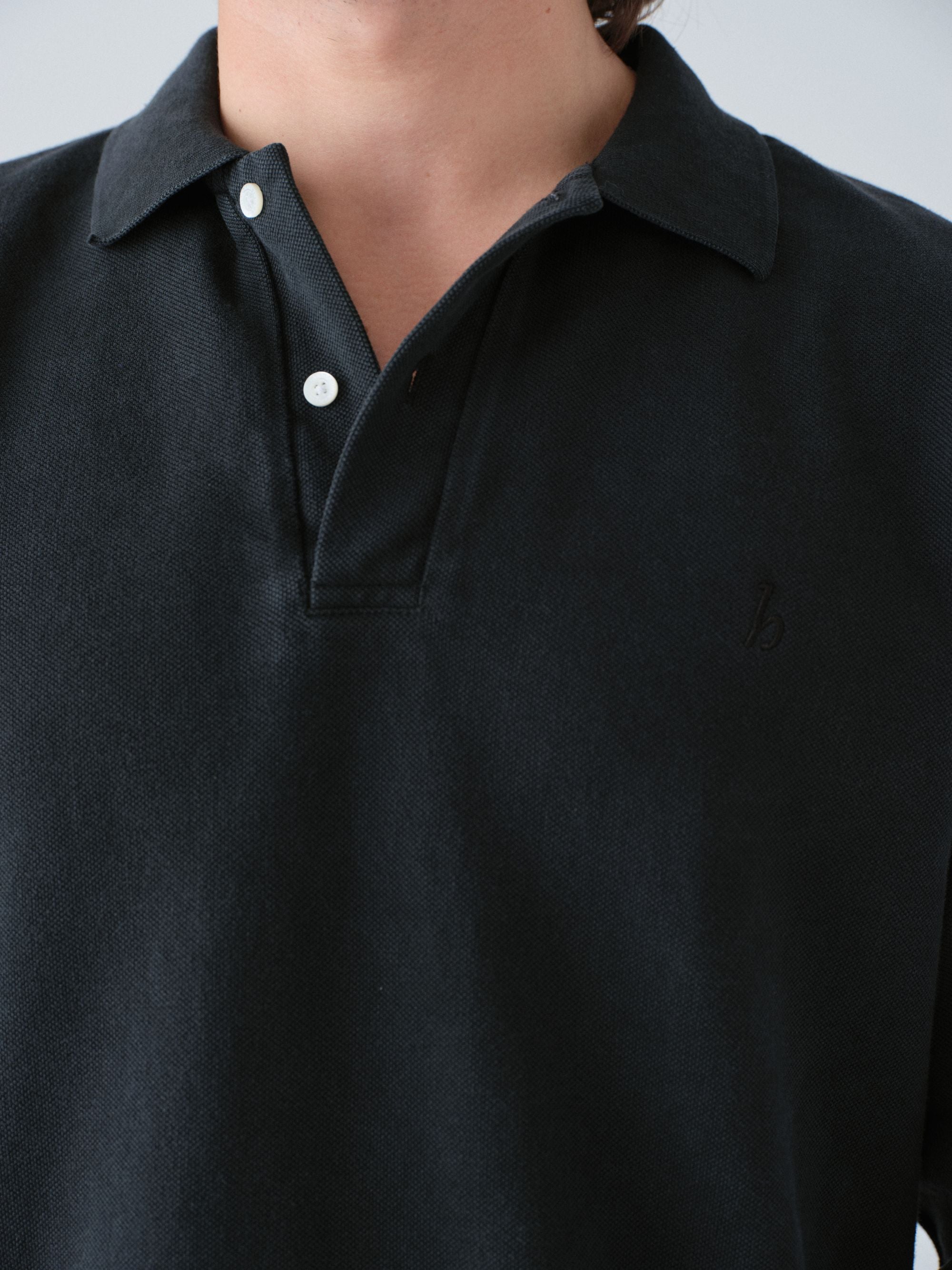 Model wearing a Sunwashed Staple Polo Shirt in vintage black color detail shot