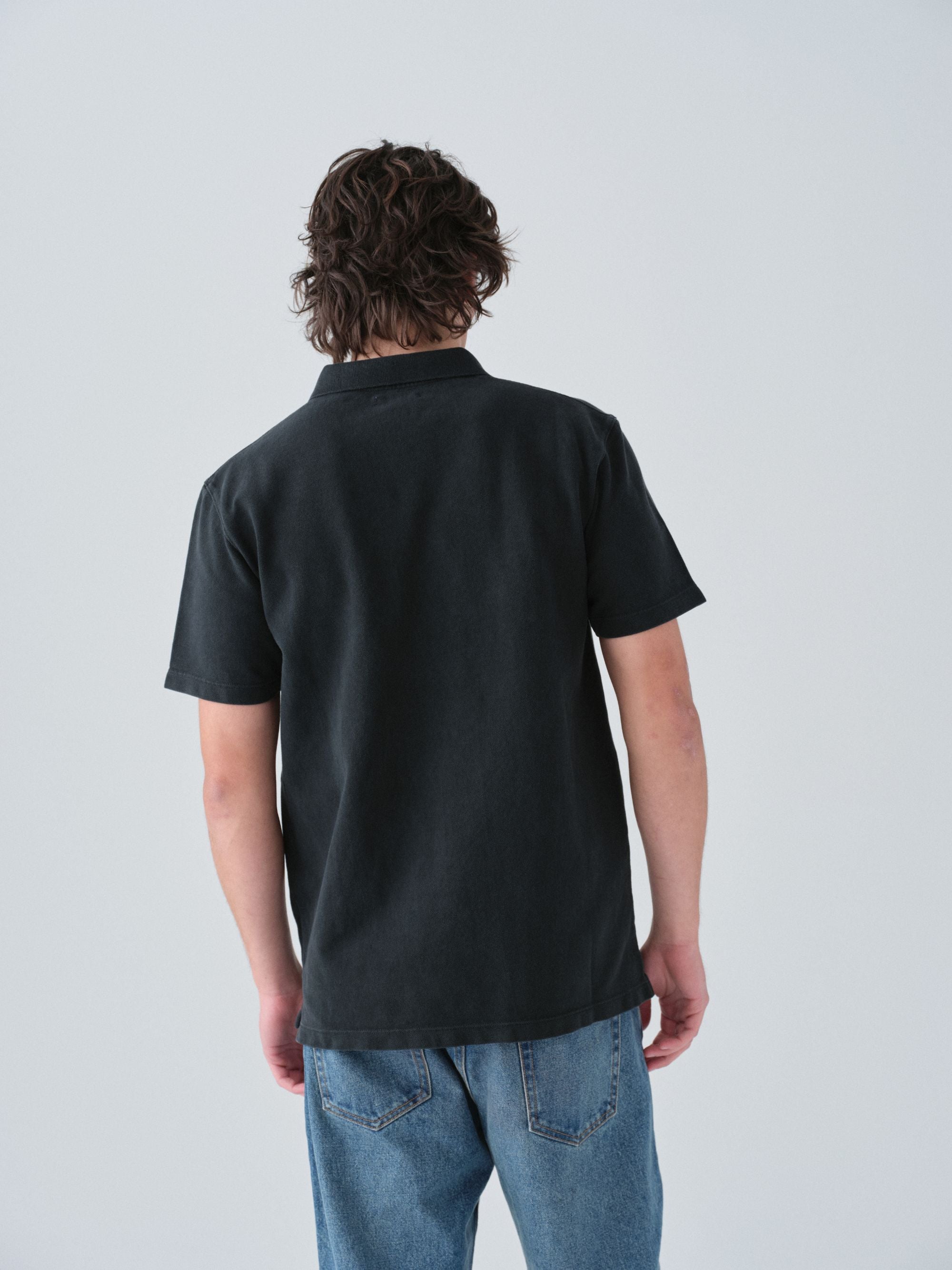 Model wearing a Sunwashed Staple Polo Shirt in vintage black color back view