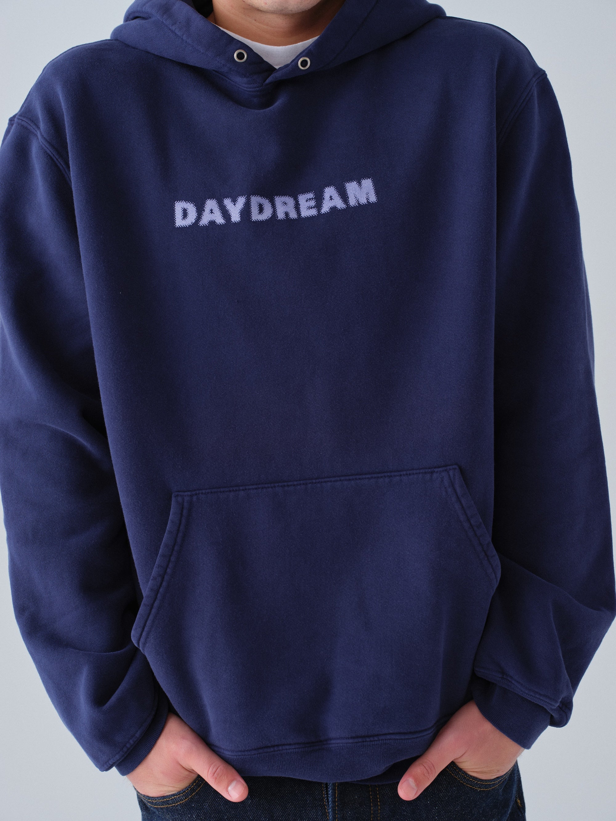 Person wearing a navy hoodie with 'DAYDREAM' text on a light gray background close up detail