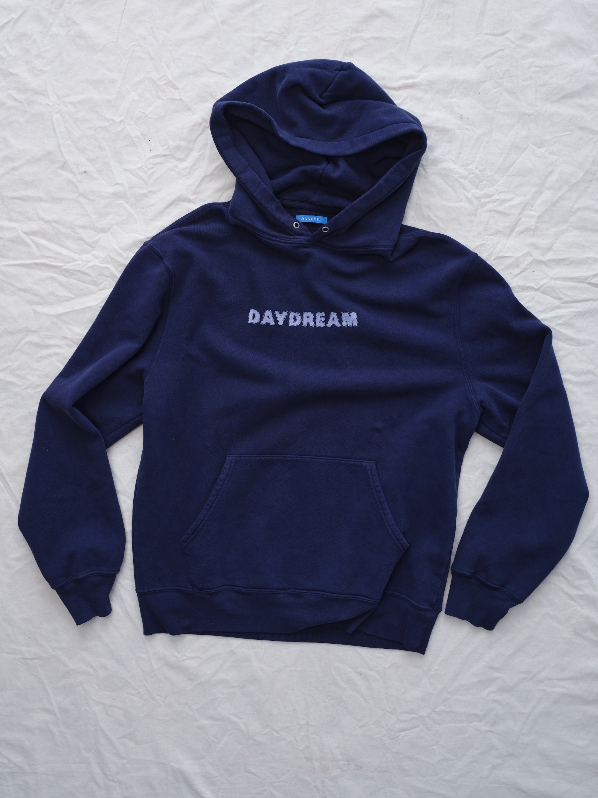 Navy blue hoodie with 'DAYDREAM' text on a light gray textured background flat lay