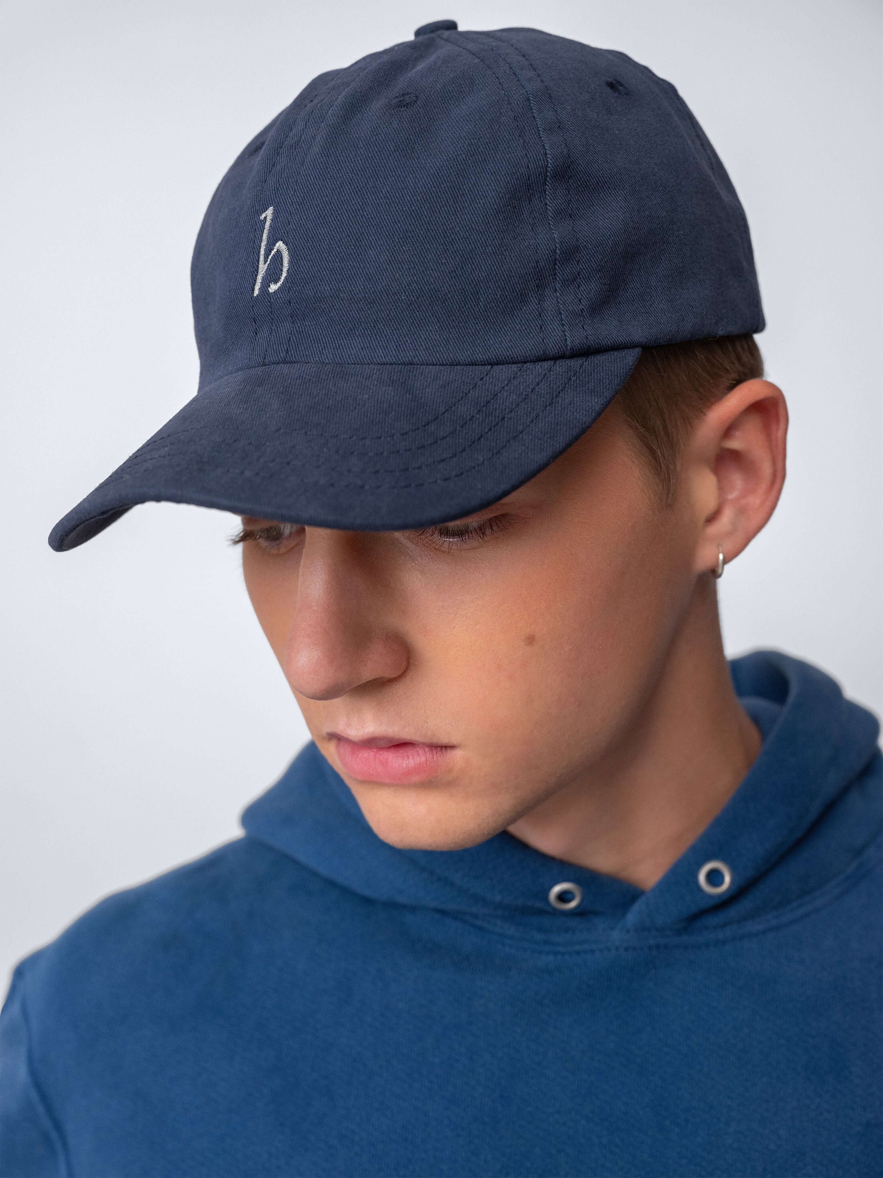 Young man wearing a Hanover Cap made from soft cotton twill, featuring embroidered logo and unstructured design.