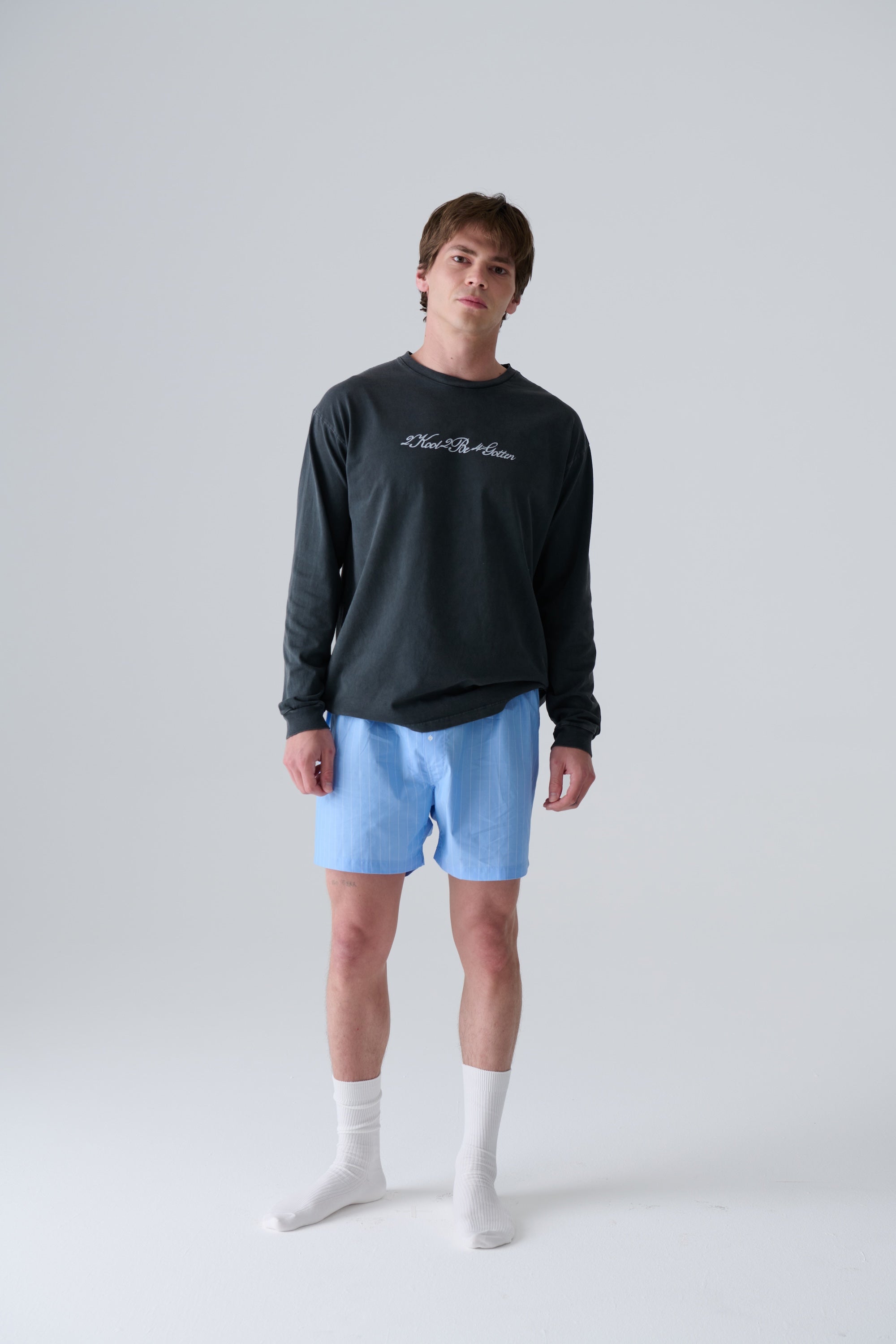 Person wearing a black long-sleeve shirt and light blue boxers on a white background