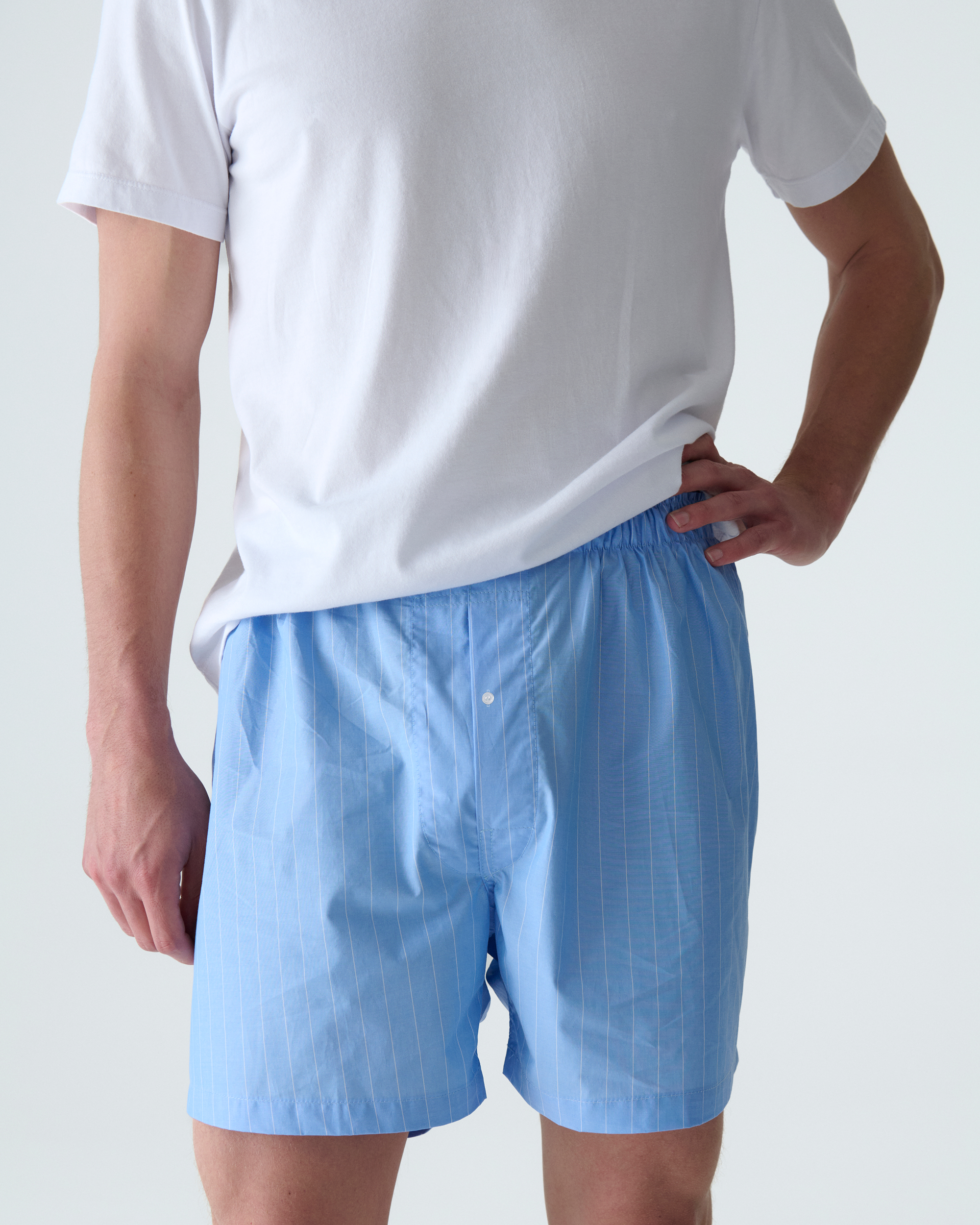 Person wearing a white t-shirt and blue striped boxers on a plain background