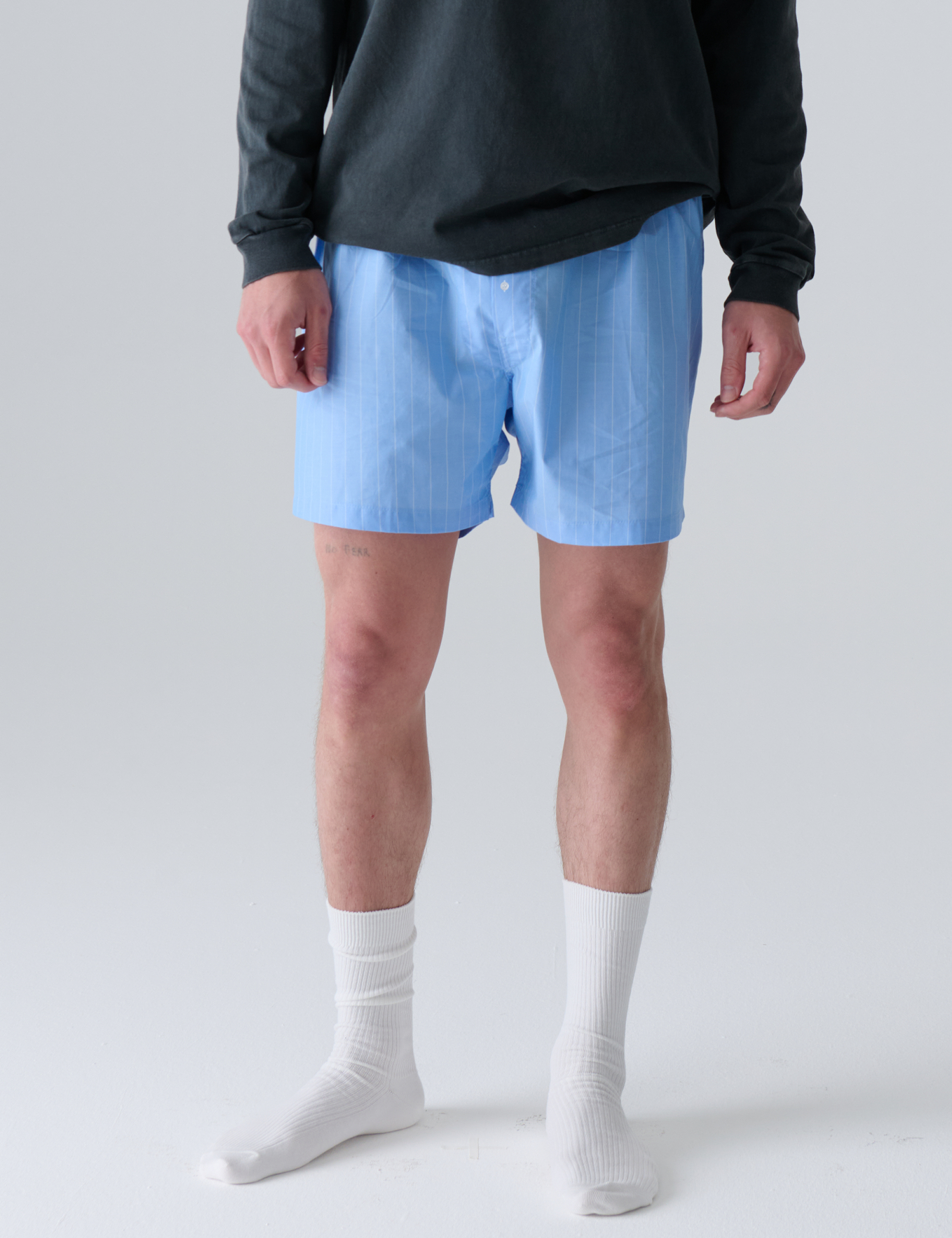 Person wearing light blue boxers and white socks on a plain background