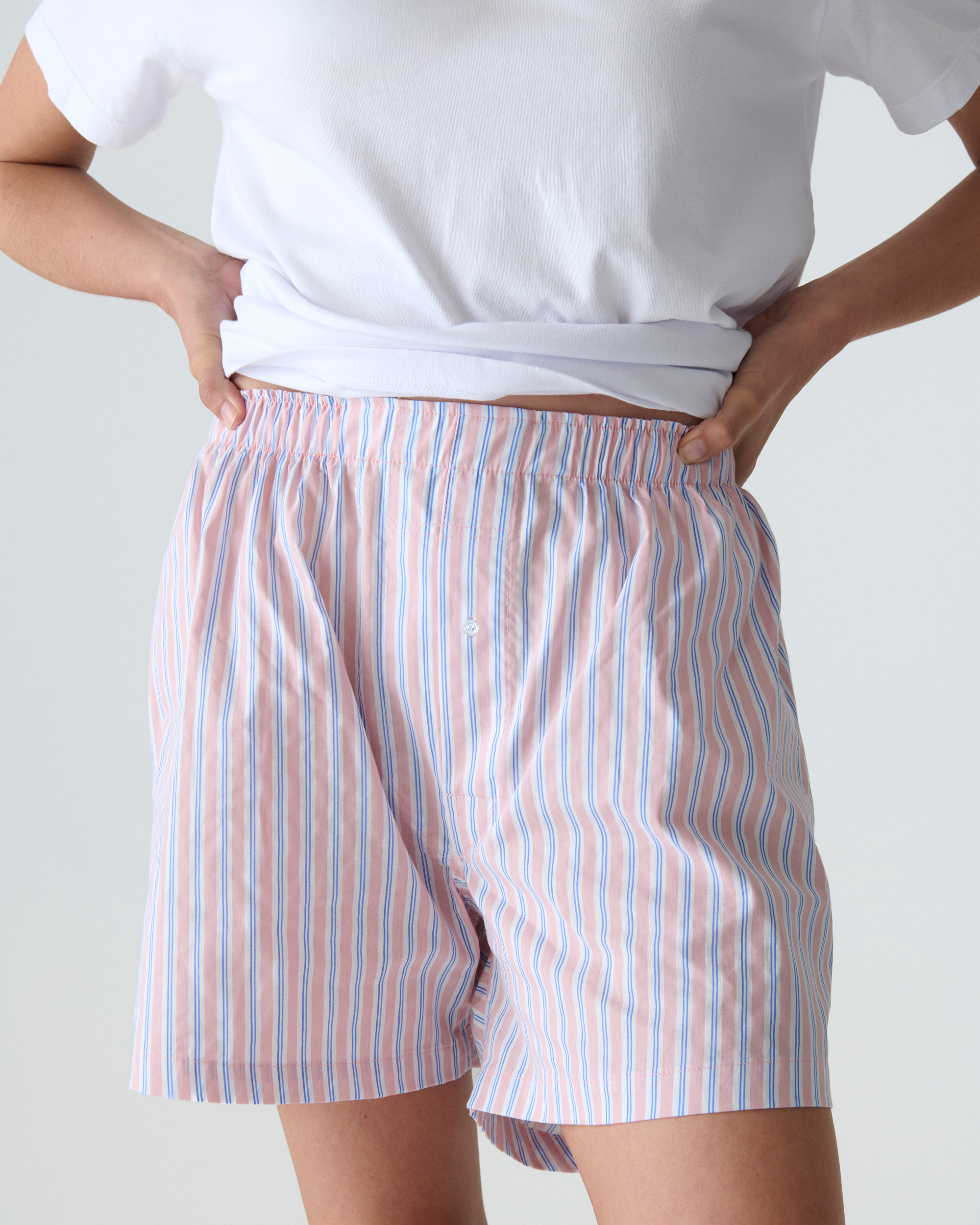 Person wearing a white t-shirt and striped boxers on a plain background