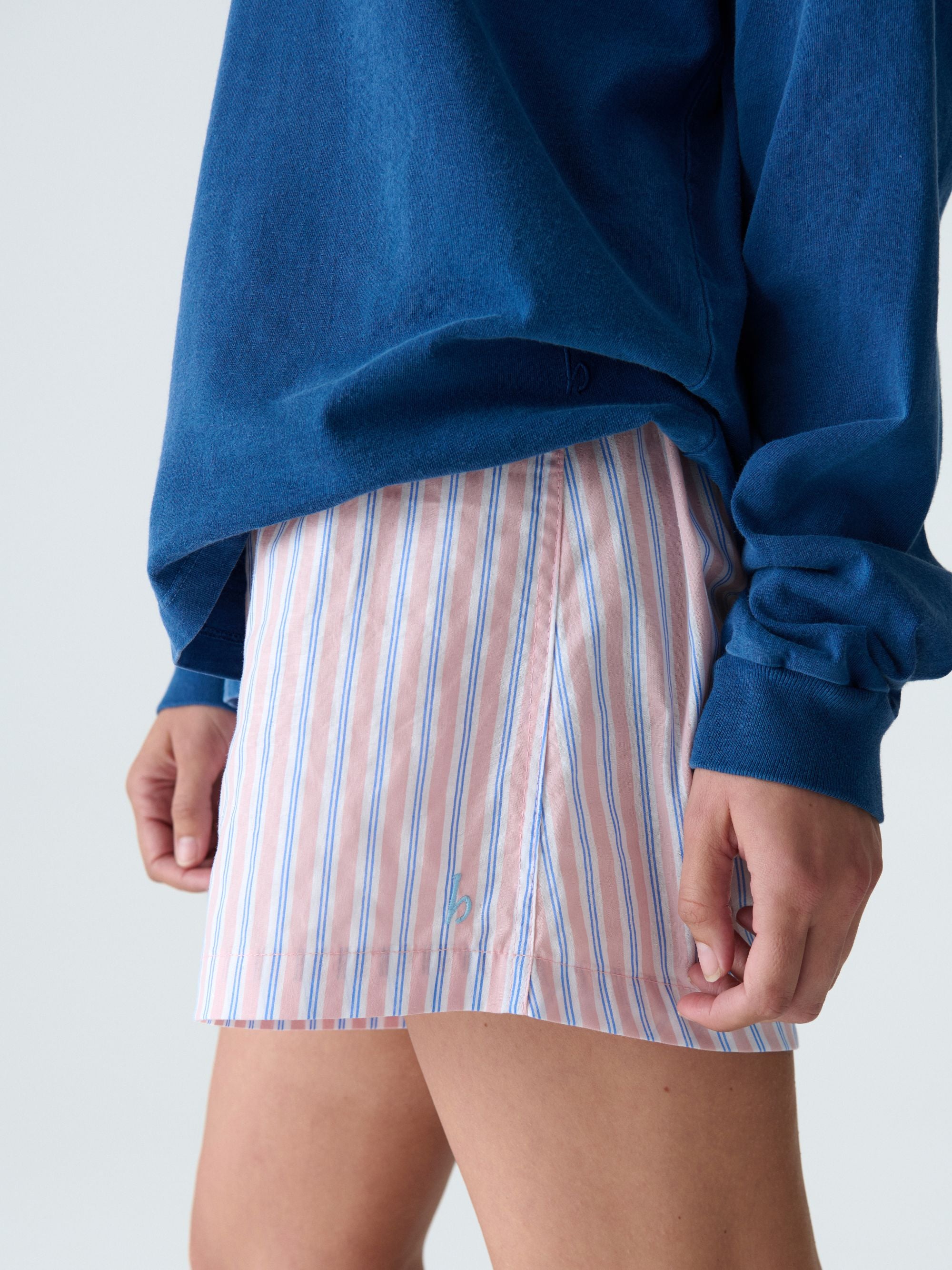 Person wearing a blue sweatshirt and striped pink and white boxers on a light gray background