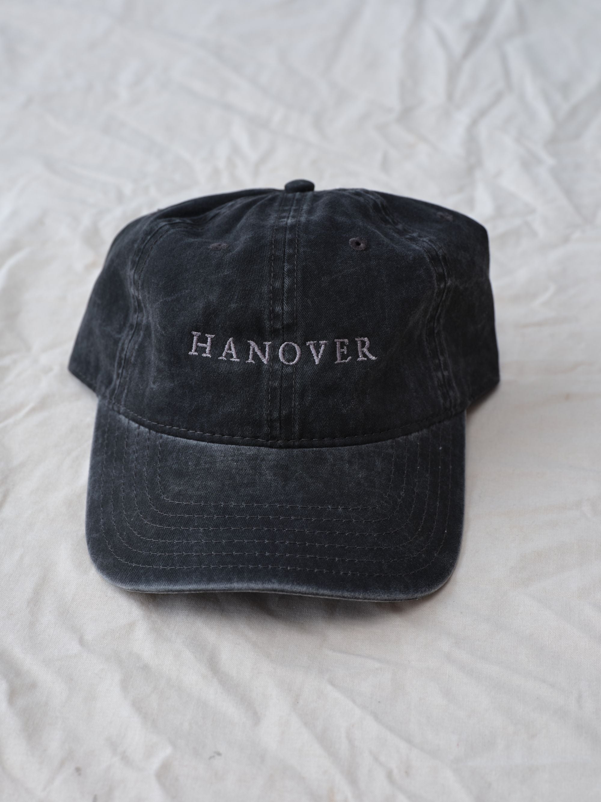 Black cap with 'Hanover' embroidery on a white textured background