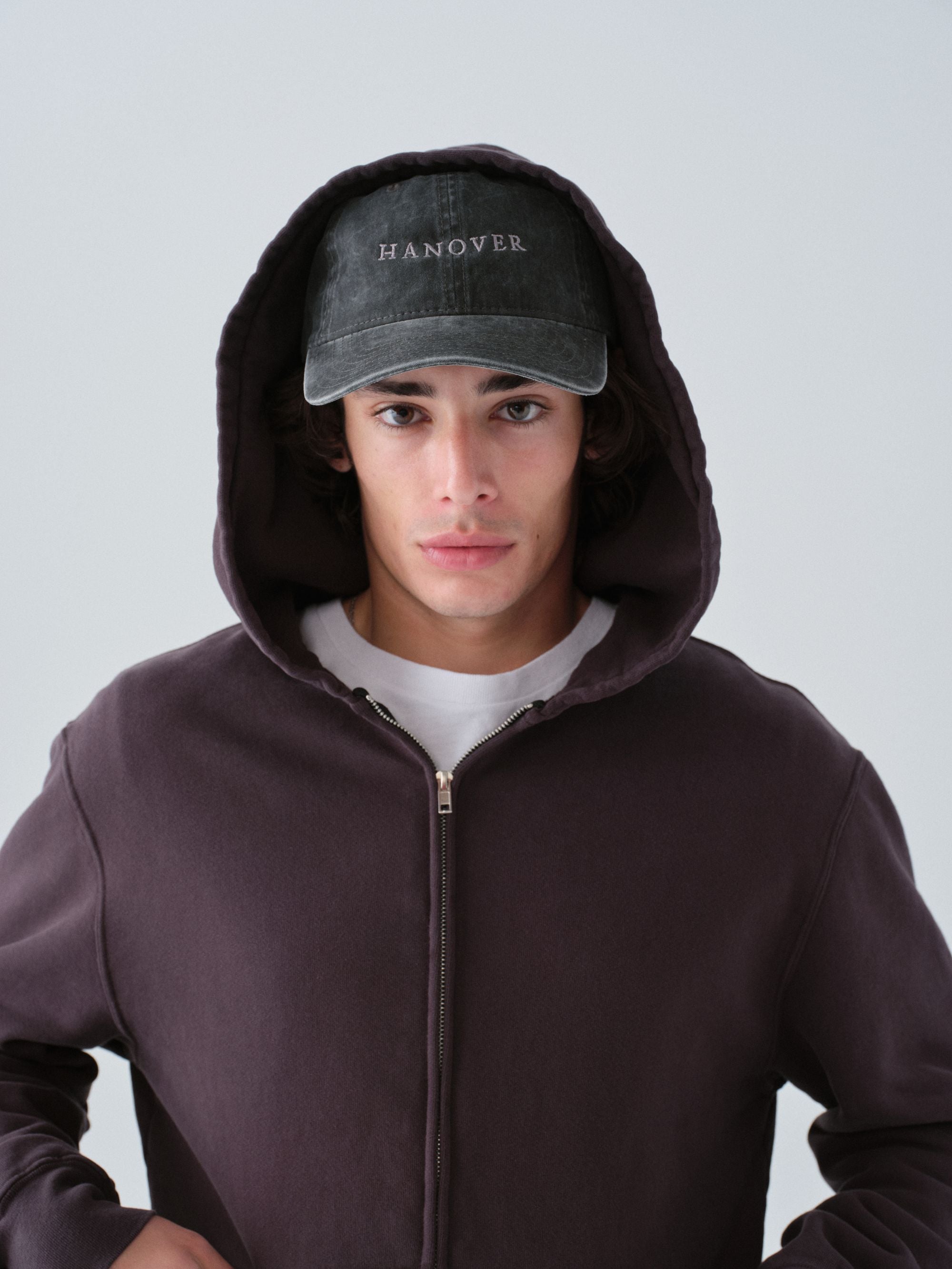 Person wearing a dark hoodie and cap with 'Hanover' text on a light gray background