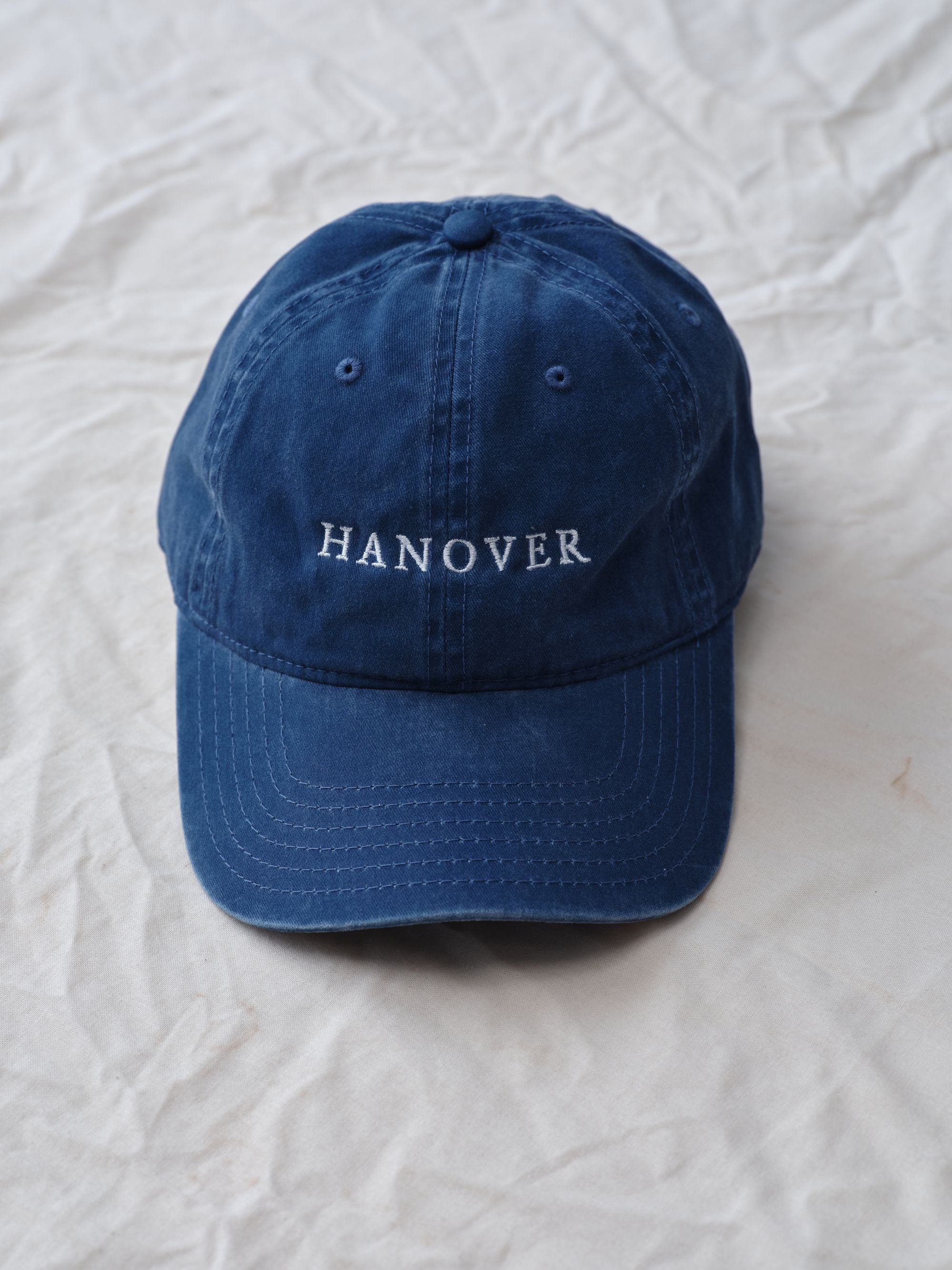 Navy blue cap with 'HANOVER' text on a textured white background