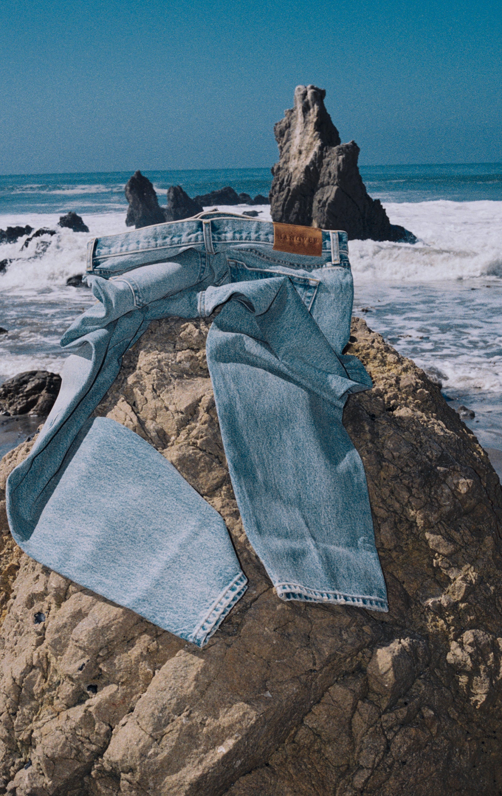 Light wash Drift denim jeans on a rocky beach with ocean and sky in the background
