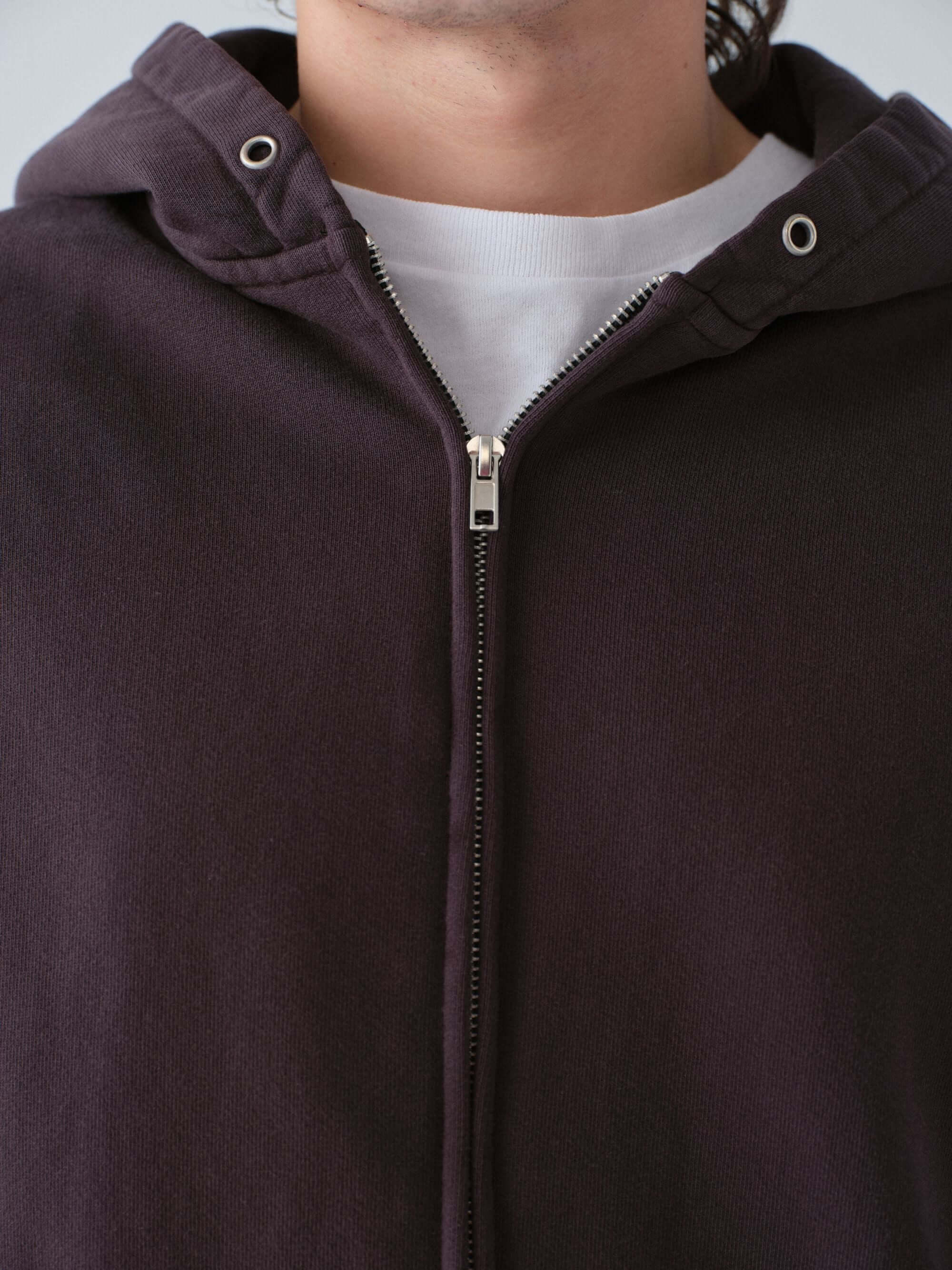 Close-up of a person wearing a  Hanover dark brown zip-up hoodie with a white shirt underneath.