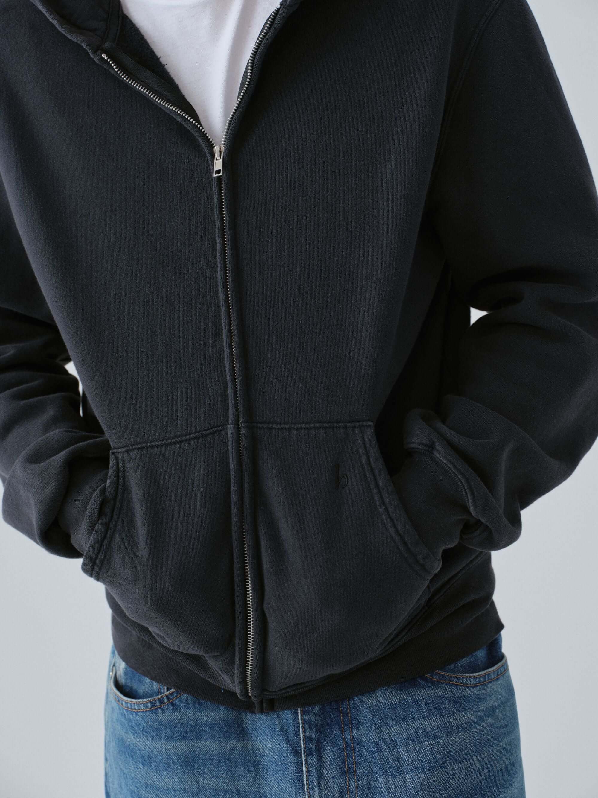 Person wearing a Hanover vintage black zip-up hoodie close up and blue jeans on a light gray background