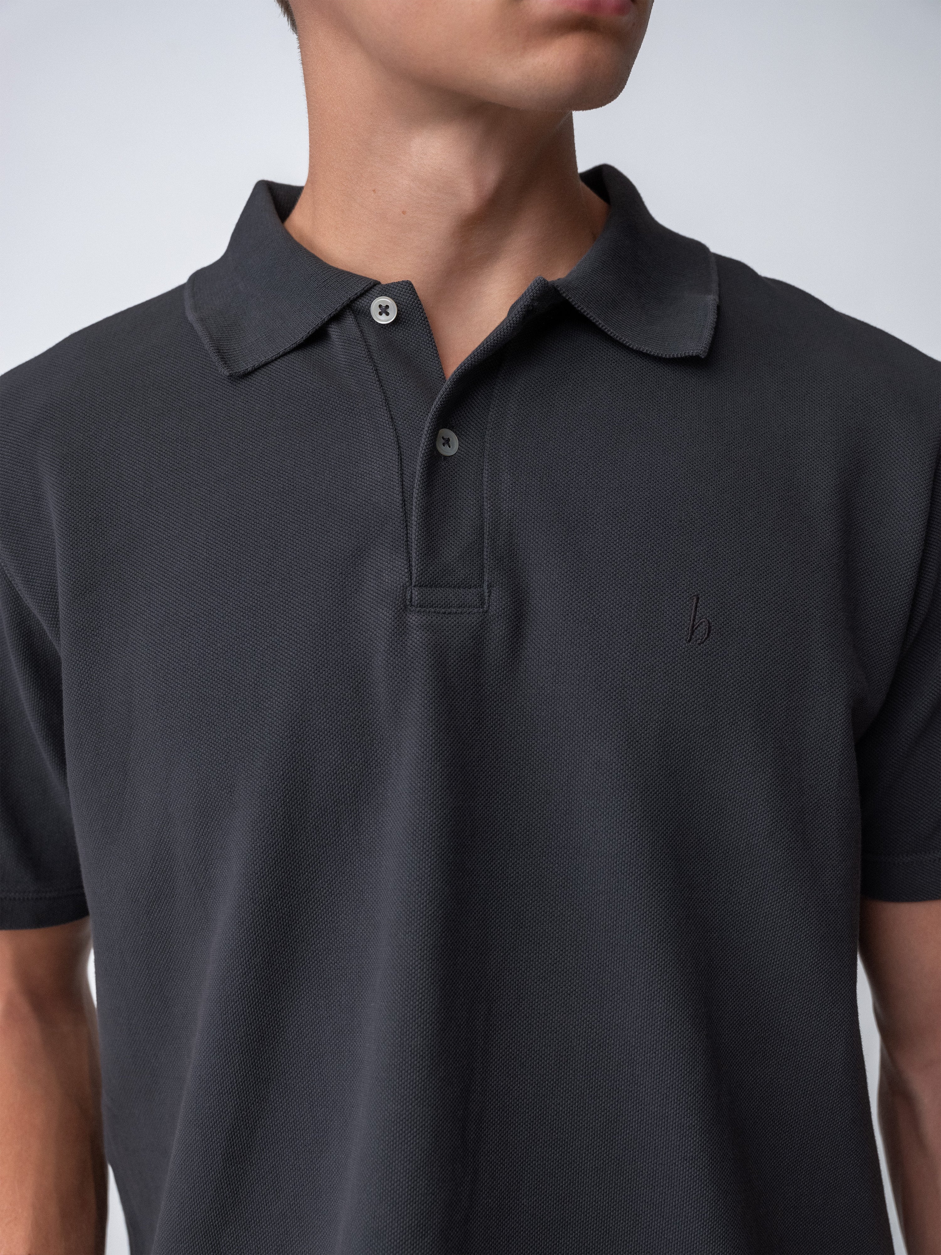 Model wearing a dark polo shirt featuring a classic collar and button closure, showcasing the Sunwashed Staple Polo shirt.